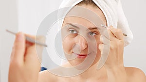 Portrait of young woman plucking eyebrows with tweezers at the bathroom mirror. Concept of beautiful female, makeup at home, skin