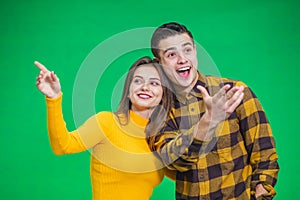Portrait of young woman pointing at something ahead isolated on green background, her boyfriend is looking at something