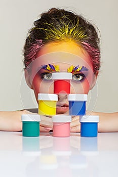 Portrait of young woman posing at the table with pyramid of small cans of paint