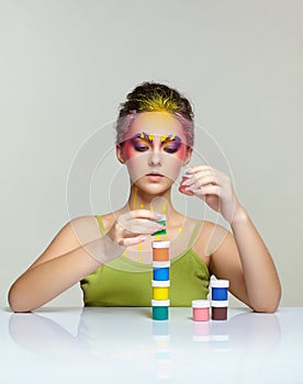 Portrait of young woman posing at the table with pyramid of small cans of paint