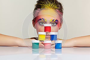 Portrait of young woman posing at the table with pyramid of small cans of paint