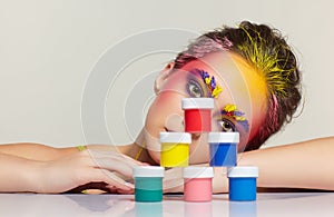 Portrait of young woman posing at the table with pyramid of small cans of paint