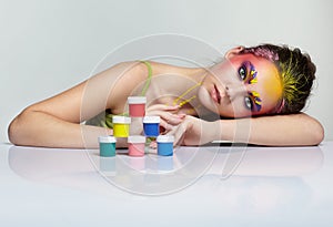 Portrait of young woman posing at the table with small cans of paint