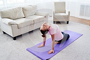 Portrait of young woman practicing yoga at home indoor, copy space. Girl stretching on mat, full length. Relaxing and doing yoga.