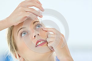 Portrait of young woman putting eye drops photo