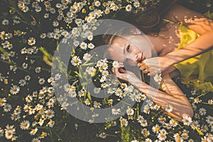 Portrait of young woman with radiant clean skin lying down amid flowers on a lovely meadow