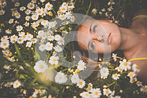 Portrait of young woman with radiant clean skin lying down amid flowers on a lovely meadow