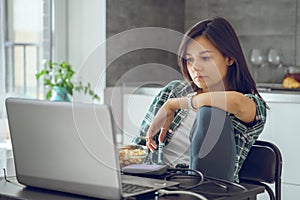 Portrait of a young woman reading news or working on a laptop in the kitchen at home. Distance work or online education