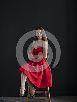 Portrait of a young woman in a red dress sitting on a high bar stool