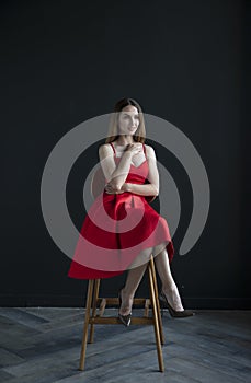 Portrait of a young woman in a red dress sitting on a high bar stool