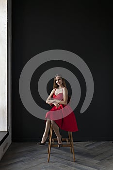 Portrait of a young woman in a red dress sitting on a high bar stool