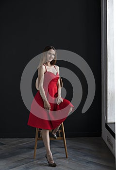 Portrait of a young woman in a red dress sitting on a high bar stool