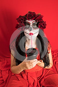 Portrait of a young woman in a red dress and traditional sugar skull makeup