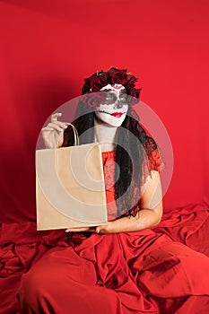 Portrait of a young woman in a red dress and traditional sugar skull makeup