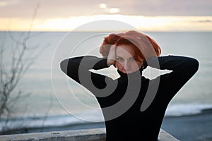 Portrait of a young woman with red hair and piercing look on the background of the sea and sunset