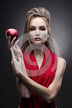 Portrait of the young woman in a red scarf with a vanguard hairstyle which holds in hand red apple on a gray background