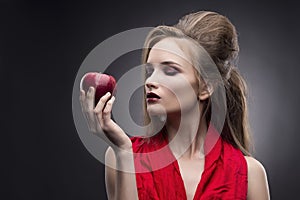 Portrait of the young woman in a red scarf with a vanguard hairstyle which holds in hand red apple on a gray background