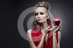 Portrait of the young woman in a red scarf with a vanguard hairstyle which holds in hand red apple on a gray background