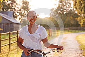 Portrait Of Young Woman Riding Bike Along Country Lane At Sunset