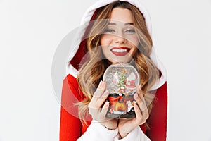 Portrait of young woman 20s wearing Santa Claus red costume smiling and holding Christmas snow ball, isolated over white