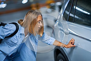 Portrait of young woman with scratched car at underground parking lot