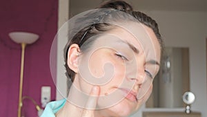 Portrait of a young woman with short hair looking at the camera, touching the skin of her face with a real pimple with