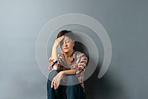 Portrait of a young woman with a short haircut who is sitting against the wall on gray empty background. Human emotions