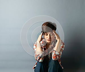 Portrait of a young woman with a short haircut who is sitting against the wall on gray empty background. Human emotions