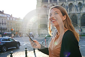 Portrait of young woman on side of road waiting a taxi cab holding a smart phone. Calling a taxi with a phone app concept