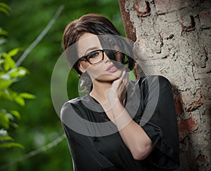 Portrait young woman with silk dressing black gown and glasses leaning against the wall and posing. Beautiful seductive