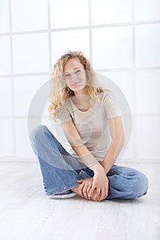 Portrait of young woman sitting on the floor dressed casual with curly and long red hair  on white window background