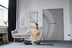 Portrait of young woman sitting at home on a mat and drinking a water