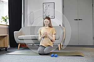 Portrait of young woman sitting at home on a mat and drinking a water