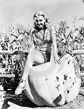 Portrait of a young woman sitting on an oversized pumpkin