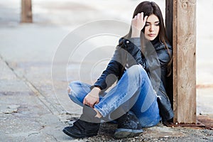 Portrait of a young woman sitting on the sidewalk.