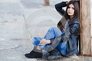 Portrait of a young woman sitting on the sidewalk.