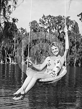 Portrait of a young woman sitting on a swing at the lakeside and smiling photo