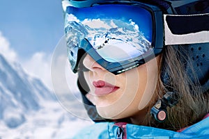 Portrait of young woman at the ski resort on the background of mountains and blue sky.A mountain range reflected in the ski mask. photo