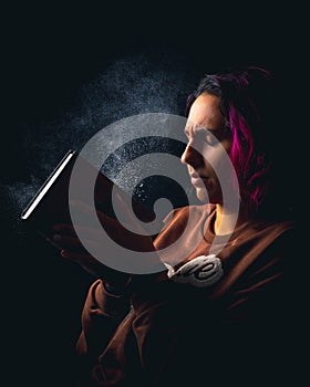 Portrait of young woman slapping a dusty book on black background low key