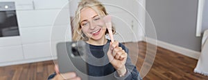 Portrait of young woman, social media influencer, taking selfies in her room, sitting on floor, holding smartphone and