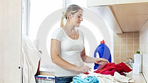 Portrait of young woman sorting piles of dirty clothes at laundry room