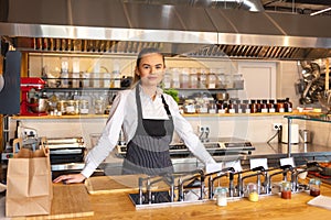 Portrait of young woman standing behind kitchen counter in small eatery