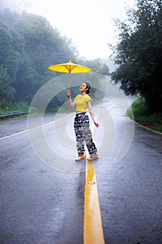 portrait of young woman standing and holding umblella in the middle of the road in the rainy season