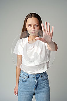 Portrait of a young woman standing with outstretched hand showing stop gesture on gray background