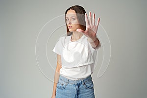 Portrait of a young woman standing with outstretched hand showing stop gesture on gray background