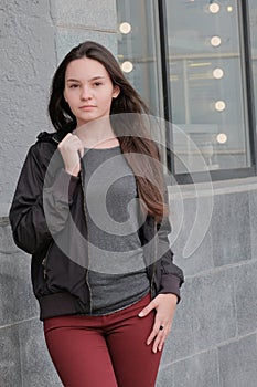 Beautiful serious girl looking at the camera. Modern fashionable style black jacket, red jeans, gray blouse. Outdoor walks in