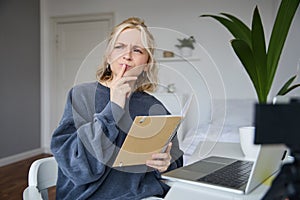 Portrait of young woman, student sitting in room, studying from home, remote education concept, holding notebook and