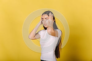 Portrait of young woman in studio has sort of a headche. Woman put hand on head. Hard working and hard day. Yellow