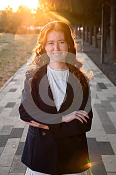 portrait of young woman in suit with waved curly red hair stands smiling in park