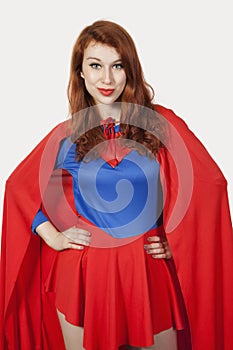 Portrait of young woman in superhero costume with hands on hips against gray background